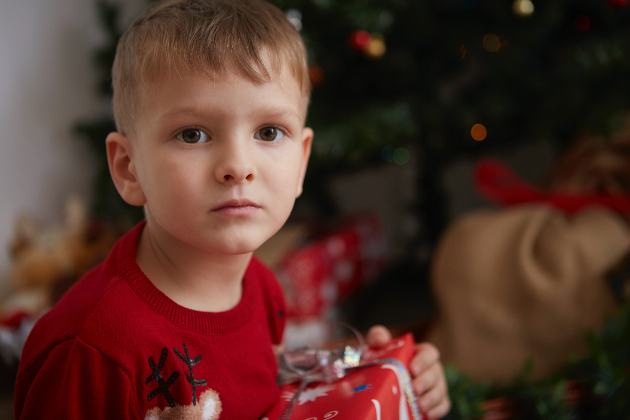 Child next to Christmas tree holding a present