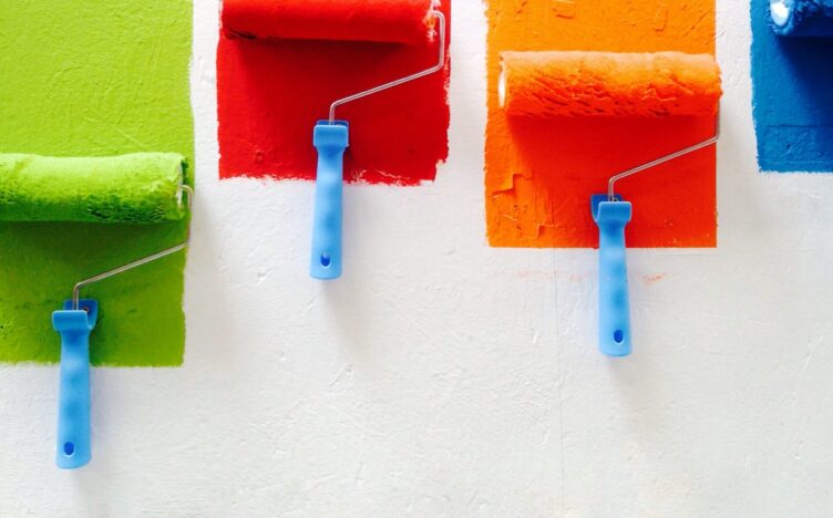 Green, red, yellow and blue pain rollers on a white wall