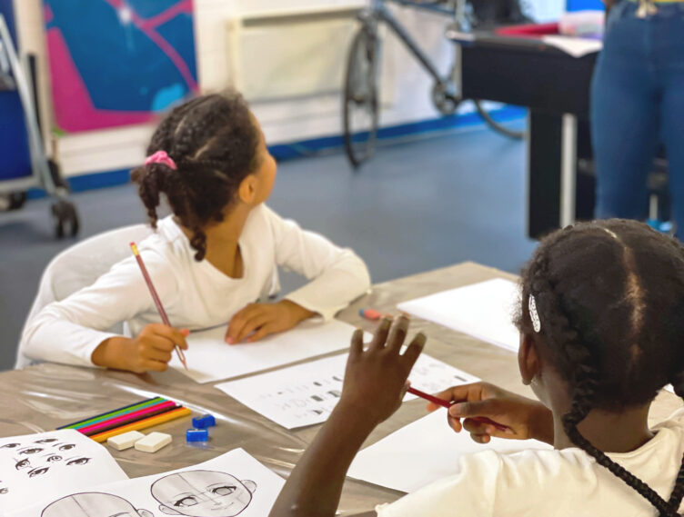 Young girls looking up at youth worker as they listen to her instructions in an anime drawing workshop