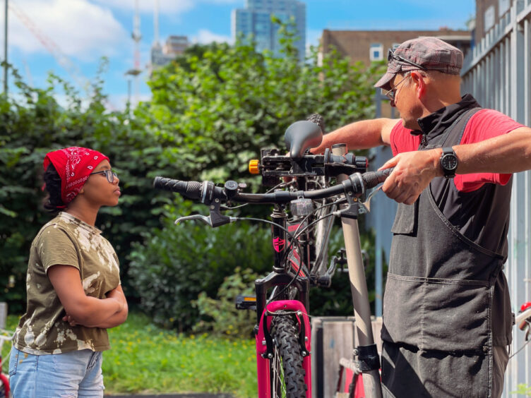 Young girl observing bike technician at work fixing her bike as part of a workshop