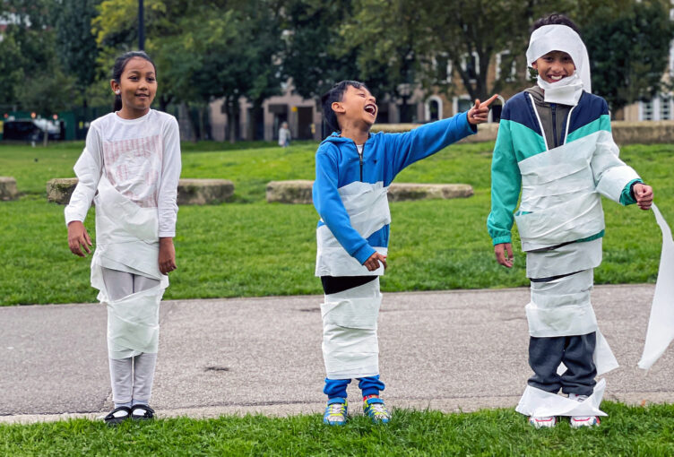 Two boys and a girl, 8-14, wrapped up in toilet paper as mummies