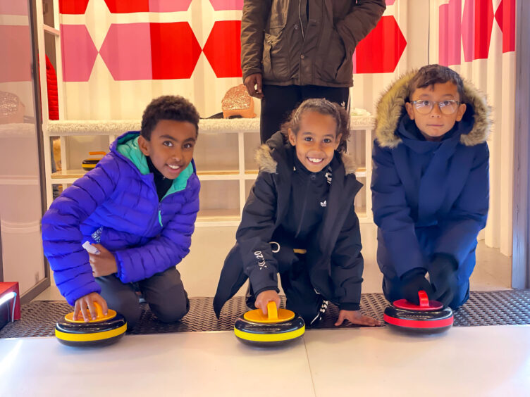 Three boys from our 8-14 group crouched down holding curling stones